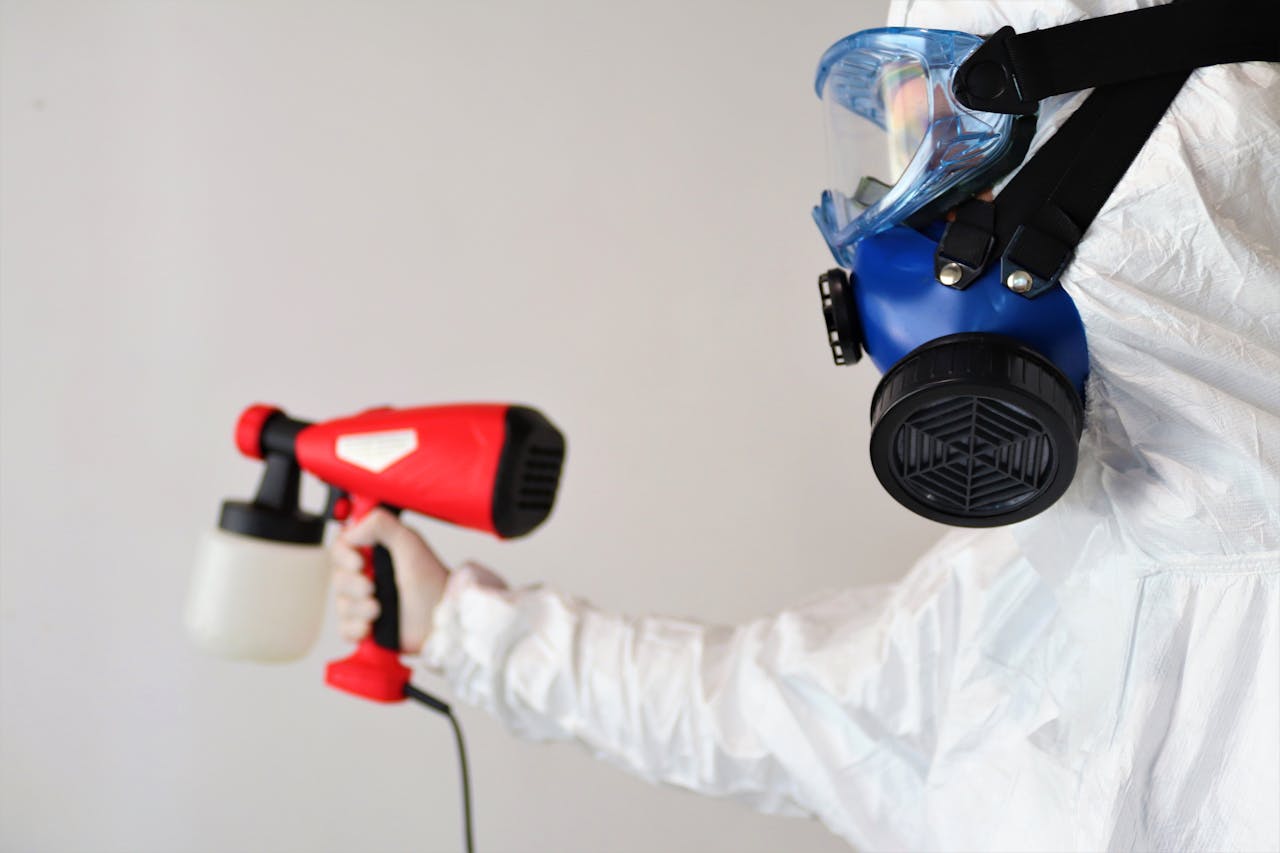 A worker in protective gear uses a disinfectant spray indoors.