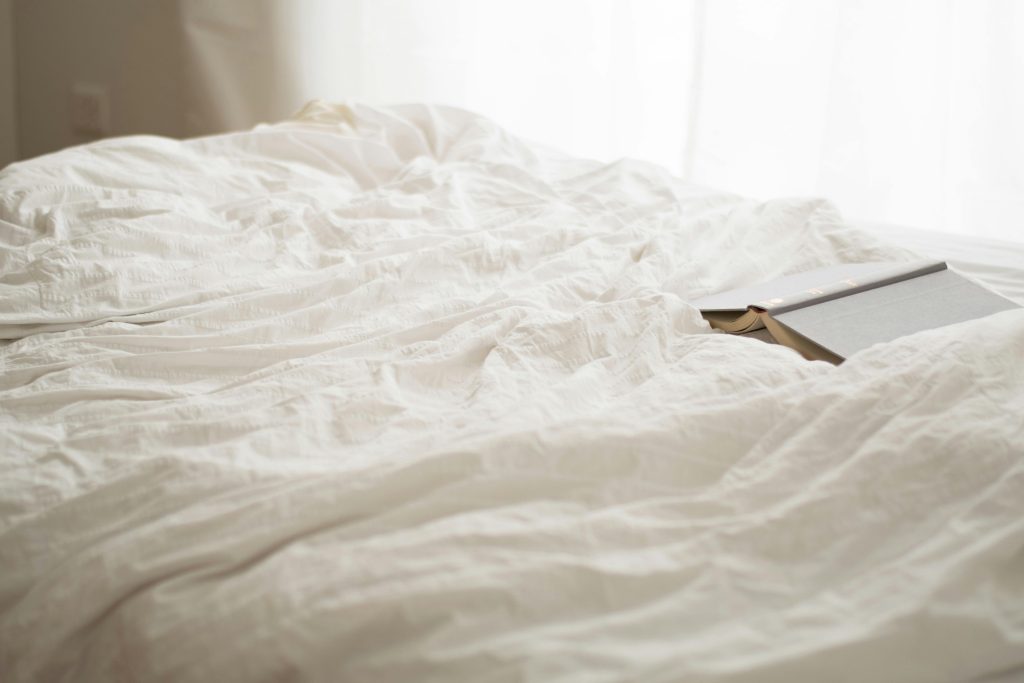 A serene bedroom scene with soft white sheets and a book, evoking relaxation and calm.