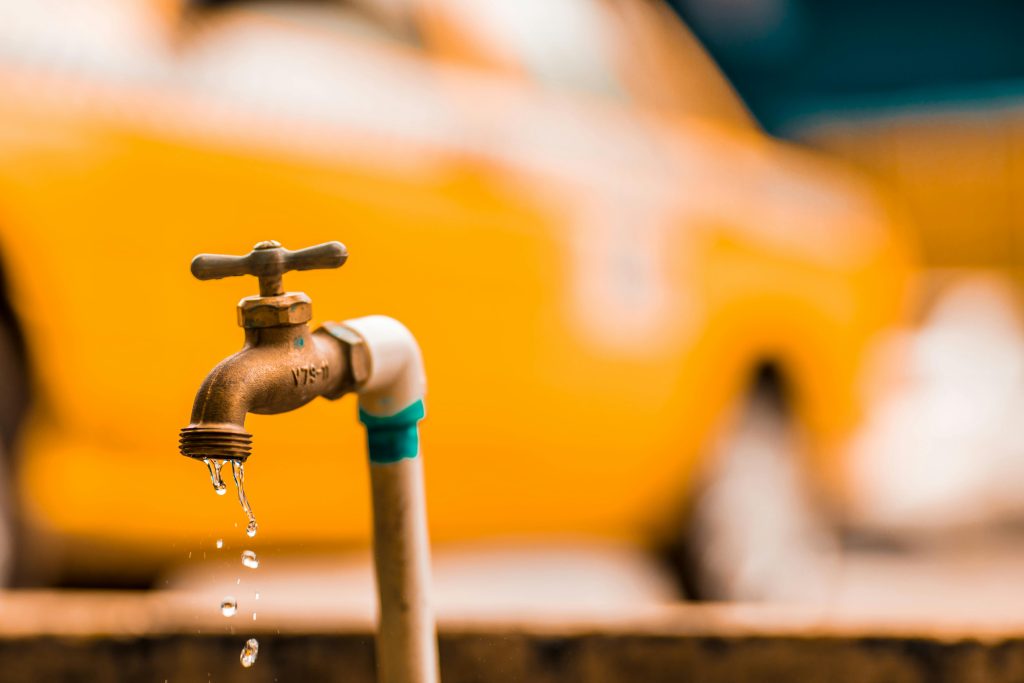 Macro shot of a brass faucet with water droplets against a blurred yellow background.