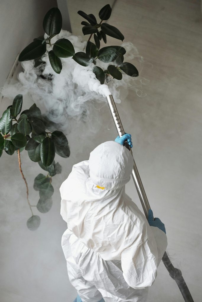 A person in protective gear uses a sprayer for indoor disinfection.